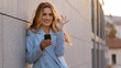 © Yuliia - Caucasian successful business woman young girl standing outdoors in city with mobile phone online shopping app smartphone chatting modern wireless device looking at camera shows ok gesture okay sign
