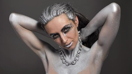 Wall Mural - Beautiful woman with silver paint on her skin and hair plays with a chain in her hands.