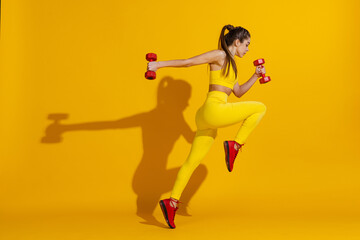 Studio shot of sportive slim girl workout with sports equipment isolated on bright yellow studio background with shadow. Beauty, sport, action, fitness, youth concept.