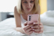 © H_Ko - Woman lies in bed and looks at smartphone closeup
