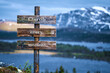 © Jon Anders Wiken - cherish every moment text quote written on wooden signpost outdoors in nature with lake and mountain scenery in the background. Moody feeling.