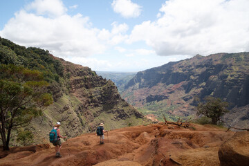 Two hikers on a red rock ledge over a canyon