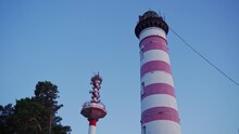 The Lighthouse Is White With Red Stripes And Next To It Is An Antenna For Communication With Ships