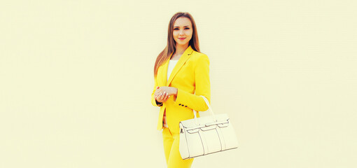 Wall Mural - Beautiful young woman wearing yellow suit with handbag posing on white background, street fashion