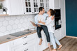 © shunevich - Joyful stylish husband and wife using laptop, watching funny videos or photos, smiling. Happy family couple are standing at the kitchen at home doing online shopping or chatting with friends