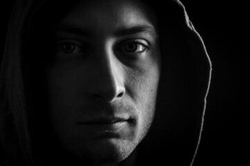 Close up portrait in black and white of a young man with a hood on his head looking grumpy in a dark atmosphere