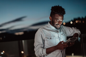 The young man on an urban city street at night texting on smartphone with bokeh and neon city lights in the background. 