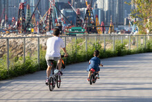 29 5 2021 Father And Son Ride Bicycles In West Kowloon Waterfront Promenade, Hong Kong. Back View. Dredger And Boats In Background