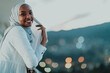 African Muslim woman in the night on a balcony smiling at the camera with city bokeh lights in the background.