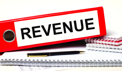 Fototapete - On the desktop are notebooks, a pen and a red folder for papers with the text REVENUE. Business concept