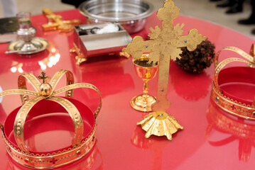 Golden cross, crowns, chalice, and paten on a red church table - wedding or baptism ceremony