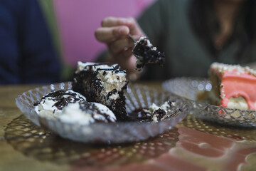 Poster - Closeup shot of chocolate cake with cream in a glass plate and a girl hand cuts cake with a fork