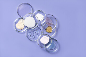 Cosmetic products, scrub, face serum and gel in many petri dishes on a violet background. Cosmetics laboratory research concept.