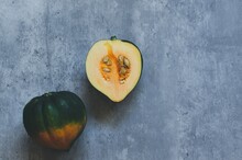 Two Halves Of A Green And Orange Acorn Squash On A Blue Grey Background