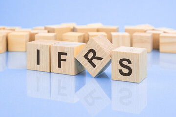 Poster - wooden cubes with the letters IFRS the bright surface of a pale lilac table. the inscription on the cubes is reflected from the surface of the table. business concept