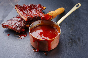 Wall Mural - Hot and spicy barbecue sauce in a casserole as close-up with spare ribs in background