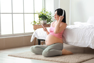 Wall Mural - Young pregnant woman listening to music in bedroom