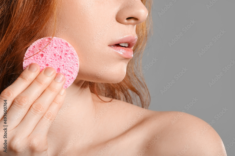 Beautiful woman with makeup sponge on grey background, closeup
