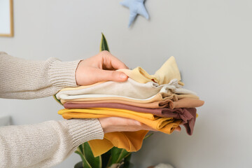 Woman with stack of baby clothes at home, closeup