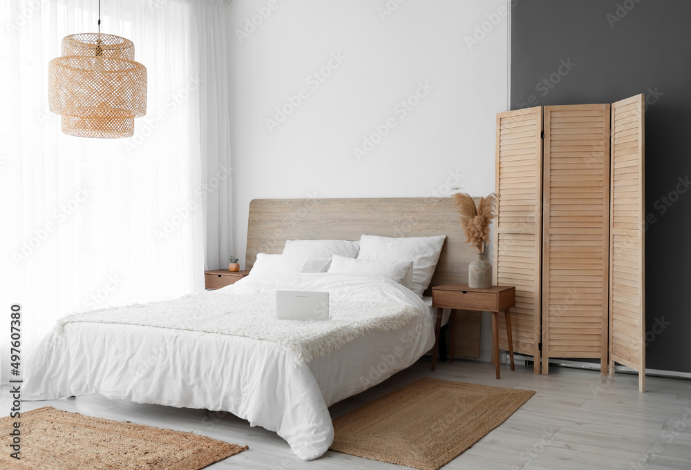 Interior of stylish bedroom with folding screen and wicker rugs