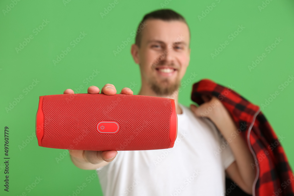 Man showing wireless portable speaker on green background, closeup