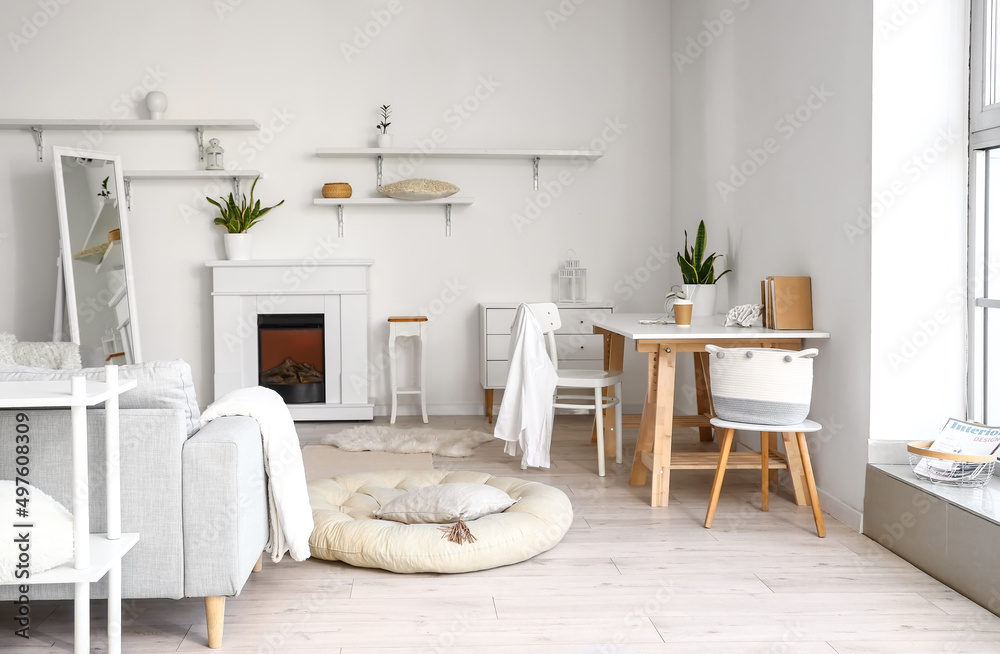 Interior of room with comfortable workplace, sofa and fireplace near white wall