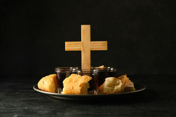 Tray with glasses of wine, bread and cross on dark background