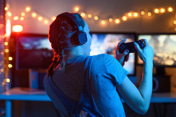 A gamer or a streamer girl at home in a dark room with a gamepad playing with friends on the networks in video games. A young man sits in front of a monitor or TV.