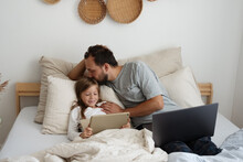 Father Kissing Daughter With Tablet On Bed