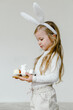 © Sergey Narevskih/Stocksy - Blonde cheerful kid with Easter eggs and in bunny ears