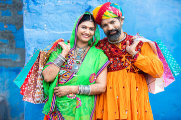 Portrait of happy traditional Indian couple holding shopping bags against blue wall background.Concept for discounts, sale, black friday.