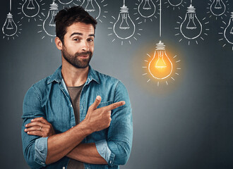 Sticker - An idea is the seed of creation. Studio portrait of a handsome young man pointing towards an illustration of a lit light bulb against a grey background.