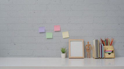 Wall Mural - Home office desk with picture frame, potted plant, stationery and colorful sticky notes on brick wall background.