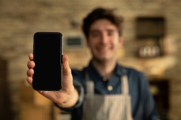 Cinematic shot of smiling artisan baker is showing in camera smartphone for online commerce applications for checking customer service and selling orders summary of baked goods in bakery shop.