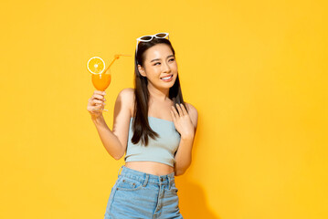 Summer portrait of pretty Asian girl with orange juice drink in isolated yellow color studio background