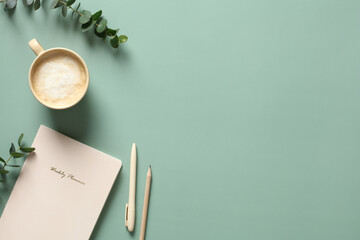 Fototapete - Modern home office desk table with paper notebook, cup of coffee, pen, pencil and eucalyptus leaves on green background. Minimalist style