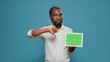 © DC Studio - Young freelancer holding horizontal green screen in studio, standing over blue background. Male entrepreneur showing blank copy space with isolated mockup template and chroma key on display.