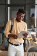 © Mediaphotos - Smiling young Black guy with satchel checking information on tablet in coworking space