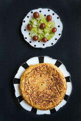 Two dishes, one Spanish omelette, and one green salad with roman lettuce, and cherry tomatoes with a black background