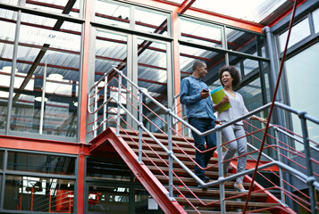 Poster - Communication is the key to success. Two colleagues walking side by side down stairs in their building.