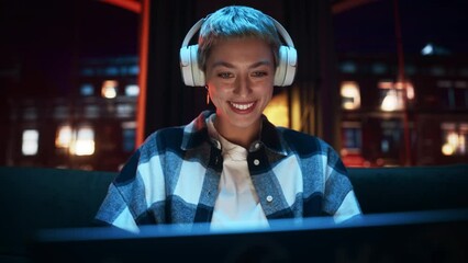 Poster - Young Beautiful Woman Wearing Headphones and Working from Home on Laptop Computer in Cozy Stylish Loft Apartment. Creative Female Smiling, Checking Social Media, Browsing Internet.  Handheld Shot.