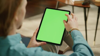 Fototapete - Young Man Scrolling and Tapping on Content on Tablet Computer with Green Screen Mock Up Display. Male Relaxing at Home, Reading Social Media Posts on Mobile Device. Close Up Over the Shoulder Footage.