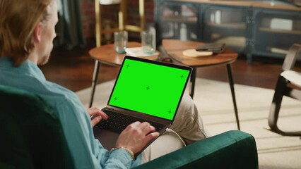 Fototapete - Young Adult Man Working from Home Loft Apartment on Laptop Computer with Green Screen Mock Up Display. Creative Male Browsing the Web, Writing on Social Media. Close Up Over the Shoulder Footage.