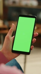 Fototapete - Vertical Screen: Feminine Hand Scrolling Feed on Smartphone with Green Screen Mock Up Display. Female Resting at Home and Checking Social Media on Mobile Device. Close Up Over the Shoulder Footage.