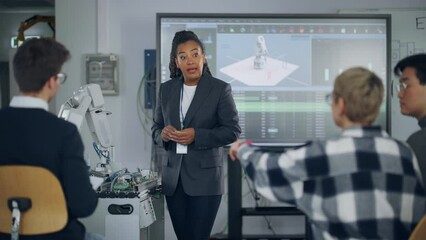 Poster - Black Teacher Asking at Students Questions and Pointing at Robotic Hand while Explaining During Lesson. Smart Girl Showing with Hand at Robot. Engineering and Programming Language Concept. Slow Motion
