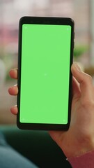 Wall Mural - Vertical Screen: Feminine Hand Scrolling Feed on Smartphone with Green Screen Mock Up Display. Female Resting at Home and Checking Social Media on Mobile Device. Close Up Over the Shoulder Footage.