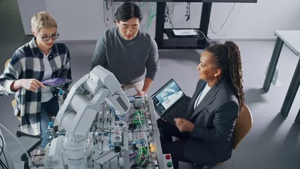 Leinwandbilder - Black Teacher Explaining Information to Students Gathering Around Table with Robot Limb. People Holding Devices with Apps and Discussing It at University. Education Concept. High Angle View