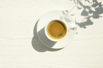 coffee cup, top view. fresh black morning coffee on a white wooden table and leaves and plant shadows