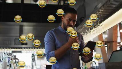 Poster - Multiple laughing face emojis against african american male bartender using digital tablet at a bar