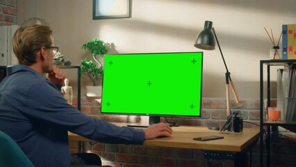 Poster - Young Handsome Man Sitting Down to Work from Home on Desktop Computer with Green Screen Mock Up Display. Creative Male Checking Social Media, Browsing Internet. Living Room in Bright Loft Apartment.